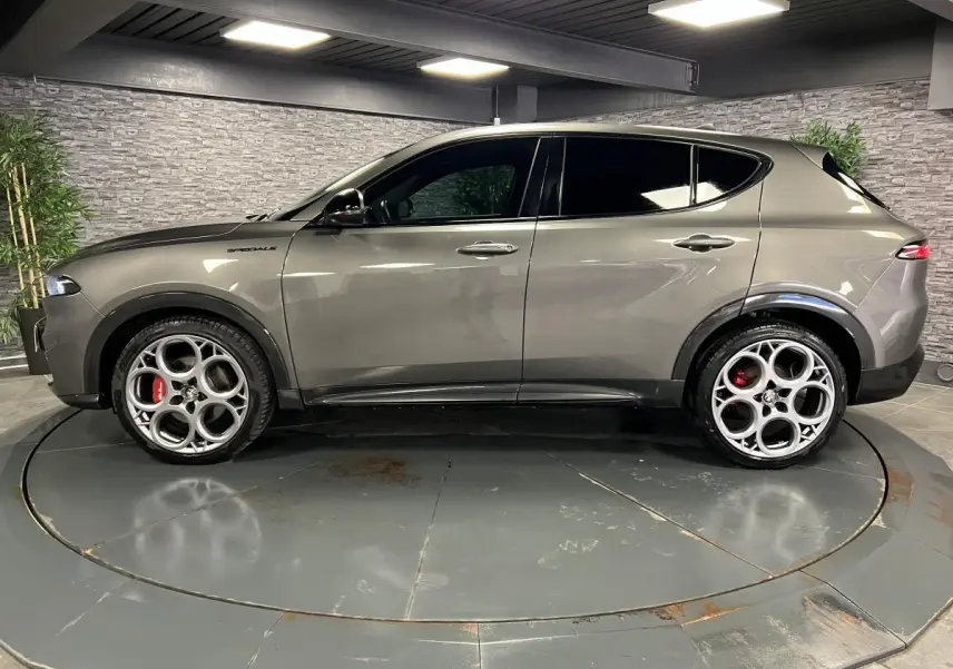 Profil droit d'un Alfa Romeo Tonale gris foncé avec jantes alliage 20 pouces et étriers de frein rouges dans un showroom.