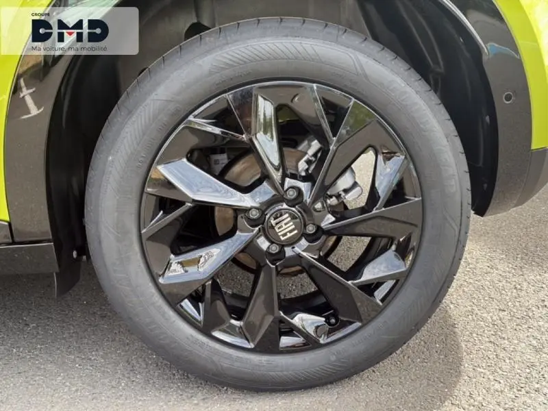 Gros plan sur la jante avant droite noire brillante de la FIAT 600 vert Méditerranéen métallisé avec logo central Fiat.