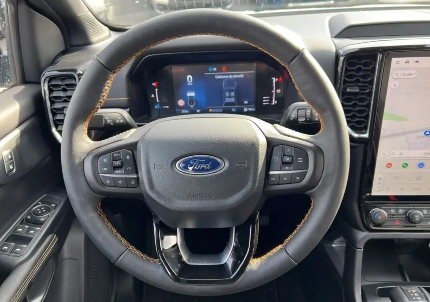 Vue rapprochée du volant cuir noir avec surpiqûres marron du Ford Ranger 2026, tableau de bord digital et écran tactile GPS.
