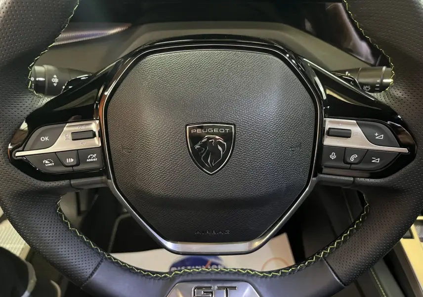 Gros plan sur le volant cuir noir perforé avec surpiqûres vertes et logo Peugeot du 308 GT PHEV 180 Hybride Rechargeable.