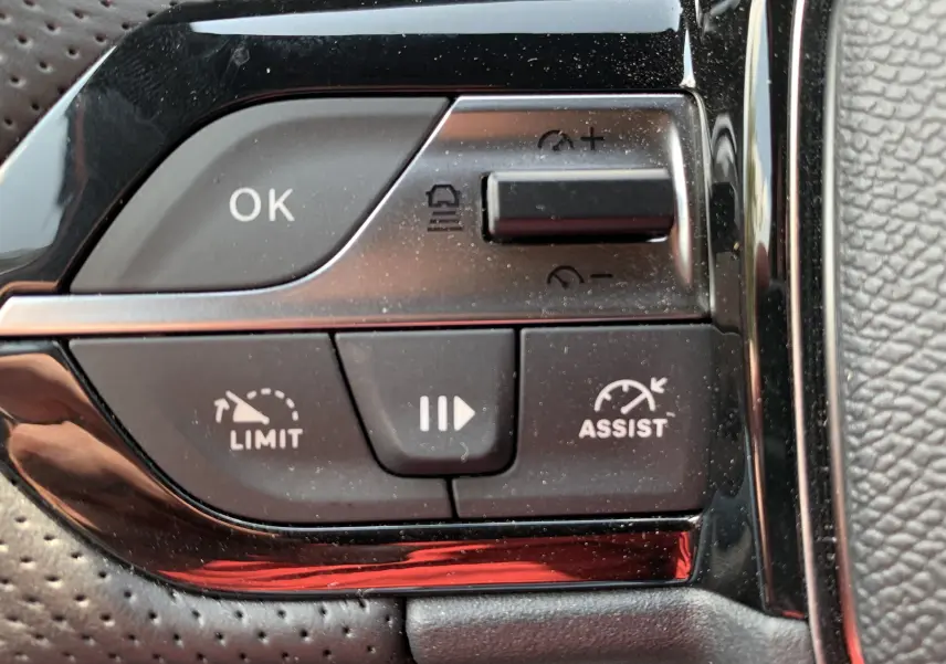 Gros plan sur les commandes au volant de la Peugeot 308 GT PHEV 180, boutons noirs avec fonction limiteur et assist.