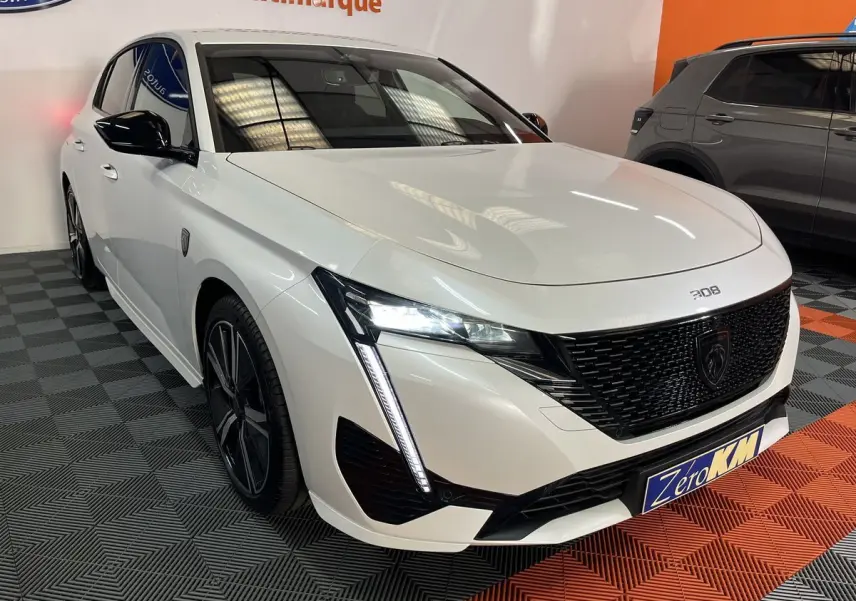 Peugeot 308 GT PHEV blanc nacré vue 3/4 avant gauche avec calandre noire et feux LED en intérieur showroom.