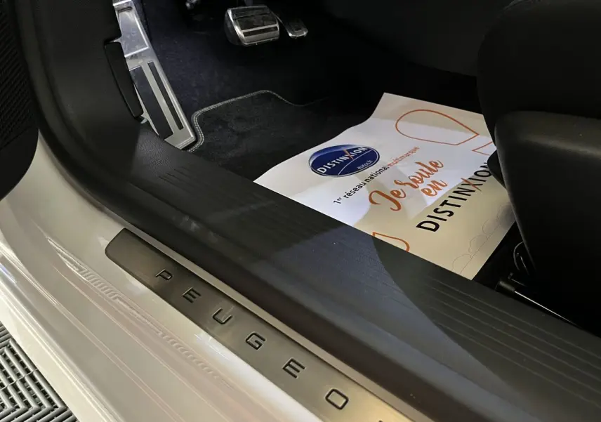 Détail intérieur côté conducteur avec seuil de porte Peugeot en métal sur carrosserie blanc nacré.
