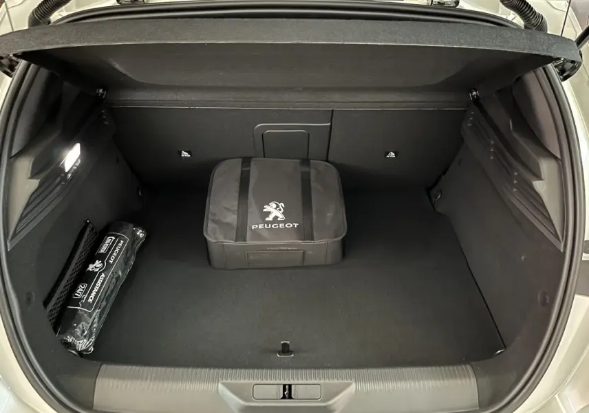 Coffre ouvert vu de l'arrière d'une Peugeot 308 GT PHEV blanc nacré avec sacoche et kit d'assistance Peugeot.