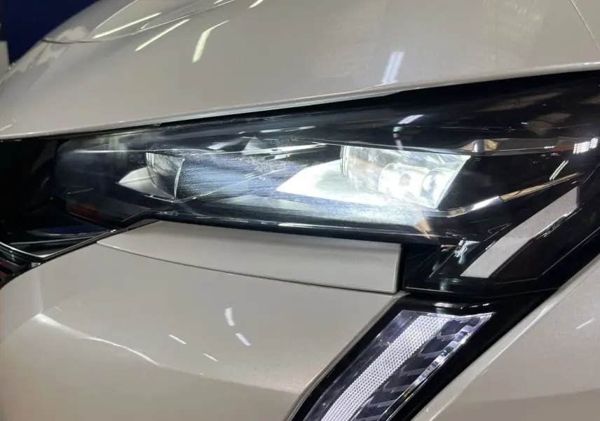 Gros plan sur le phare avant droit blanc nacré du Peugeot 308 GT PHEV 180 EAT8 avec éclairage LED allumé.