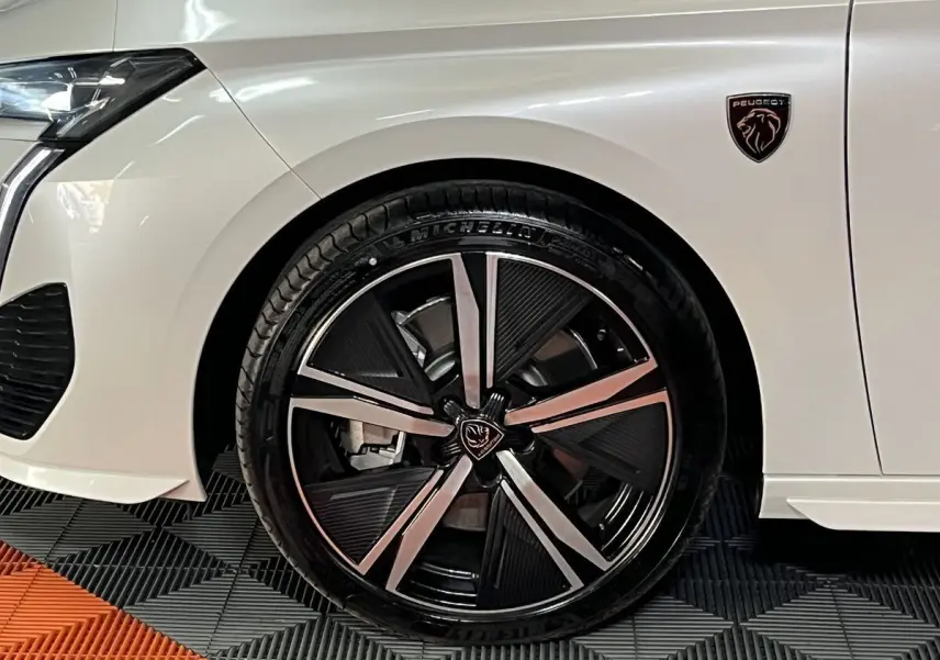 Gros plan sur la roue avant gauche et l’aile blanche nacrée d’une Peugeot 308 GT PHEV 2022 avec logo lion noir.