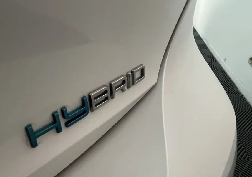 Gros plan sur l’inscription HYBRID bleue sur la carrosserie blanc nacré arrière droite d’une Peugeot 308 GT PHEV.