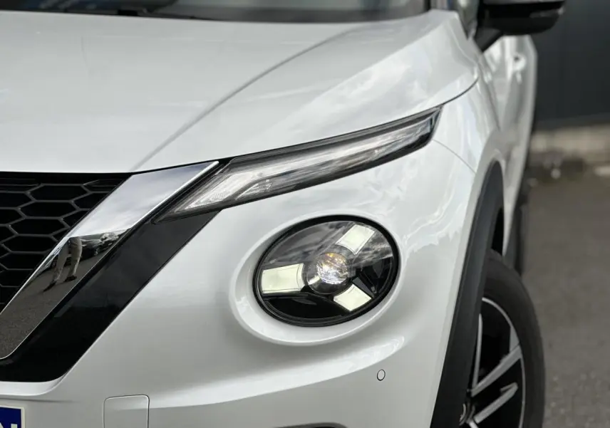 Gros plan sur l'avant droit blanc nacré du Nissan Juke 2025, mettant en valeur son phare rond et la calandre noire.