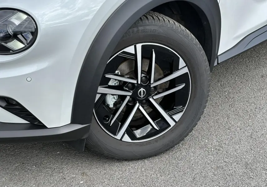 Gros plan sur la roue avant gauche du Nissan Juke blanc nacré, avec jante alliage noire et argentée design moderne.