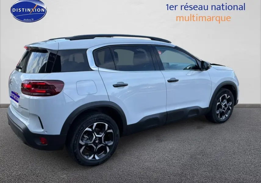 Vue 3/4 arrière droite d'un Citroën C5 Aircross blanc avec barres de toit et jantes alu noires et argentées.