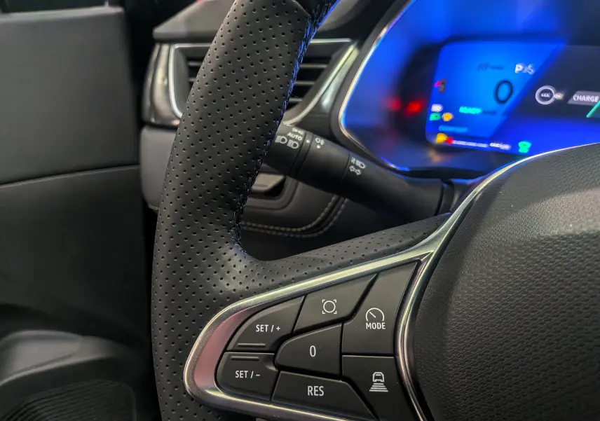 Gros plan sur le volant perforé et les commandes multifonctions d’un Renault Symbioz E-Tech noir étoilé, tableau de bord numérique bleu visible.