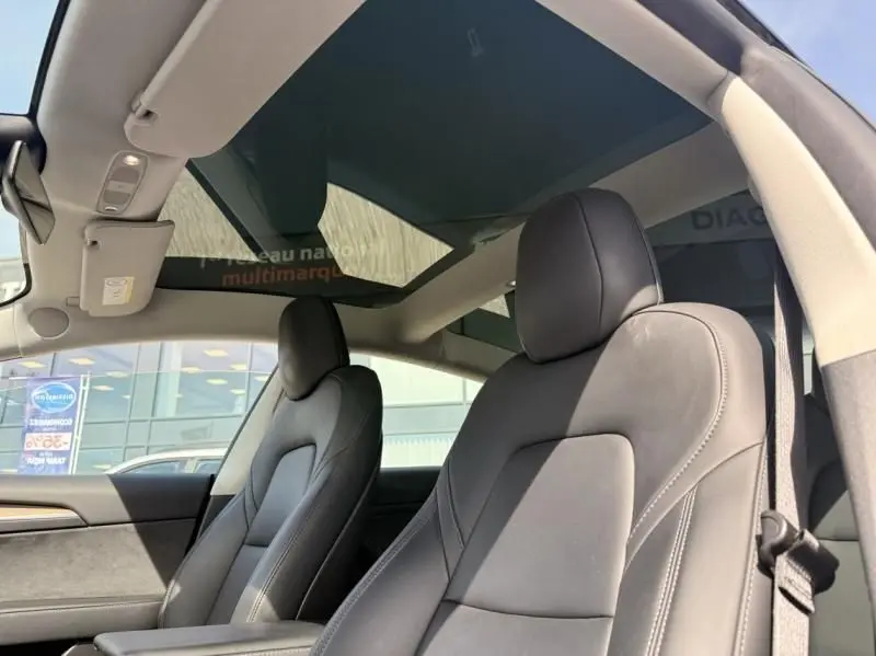 Vue intérieure de face des sièges avant noirs et du toit en verre panoramique d'une Tesla Model 3 Standard RWD Plus 2022.