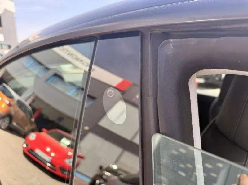 Gros plan sur la porte côté gauche d’une Tesla Model 3 noire 2022, avec reflet d’un bâtiment et d’autres voitures.