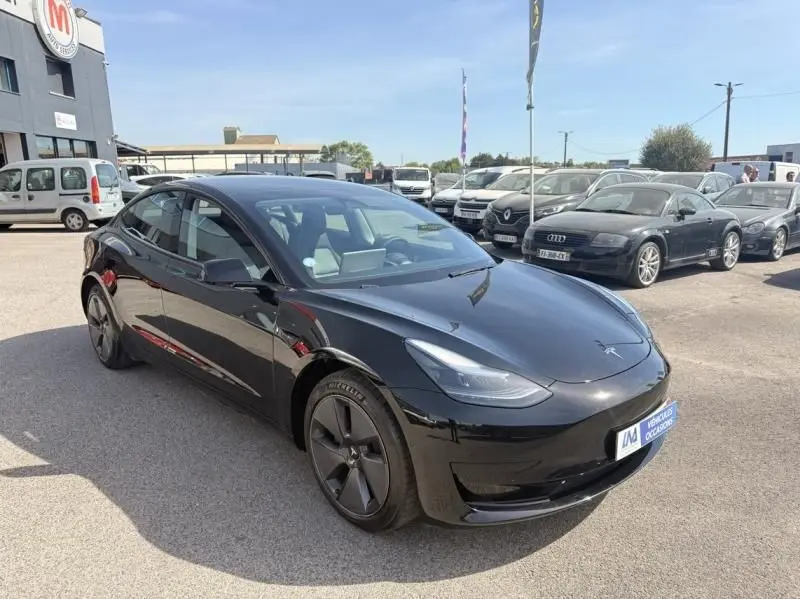 Tesla Model 3 Standard RWD Plus noir vue 3/4 avant droit, avec jantes aérodynamiques distinctives, sur parking extérieur.