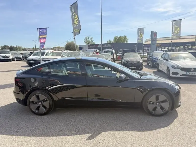 Tesla Model 3 Standard RWD Plus noir vue de profil côté gauche, avec jantes aérodynamiques distinctives, en extérieur.