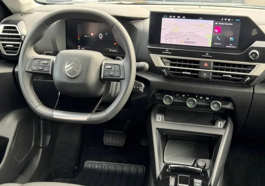 Vue intérieure avant du tableau de bord noir d'une Citroën C4 1.2 Hybride avec écran tactile et volant cuir.
