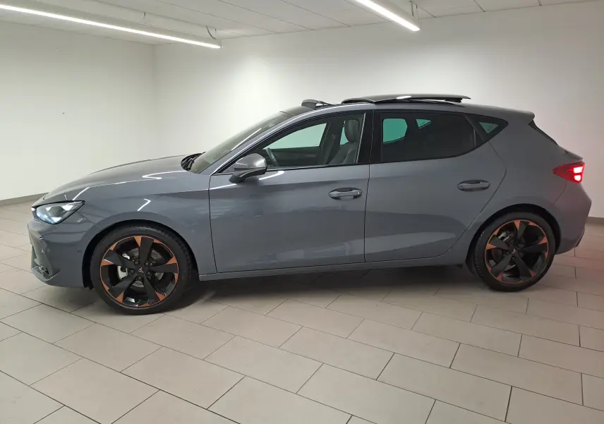 Vue de profil côté gauche d'une CUPRA Leon 2025 gris Graphène avec toit ouvrant panoramique et jantes cuivrées.