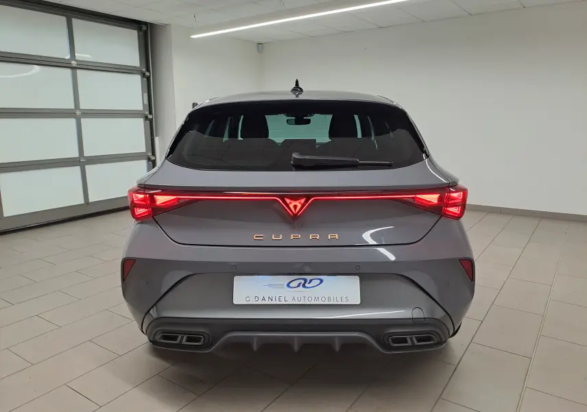 Vue arrière d'une CUPRA Leon 2025 gris Graphène avec feux LED allumés et double sortie d'échappement rectangulaire.