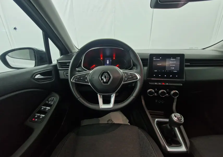 Intérieur de Renault Clio V gris platine, vue depuis le siège conducteur sur le volant, tableau de bord et levier de vitesse manuel.