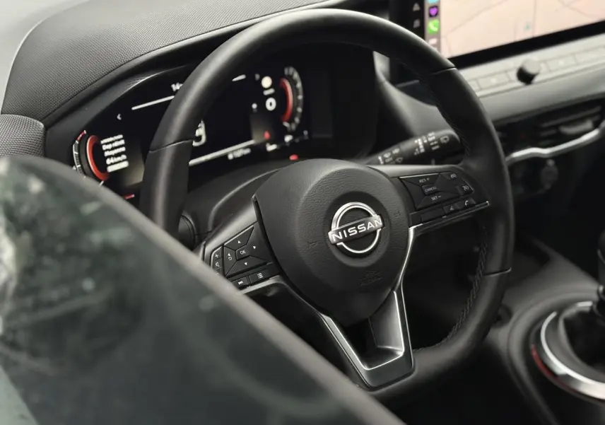 Vue rapprochée du volant en cuir noir et du tableau de bord digital du Nissan Juke blanc nacré 2025.