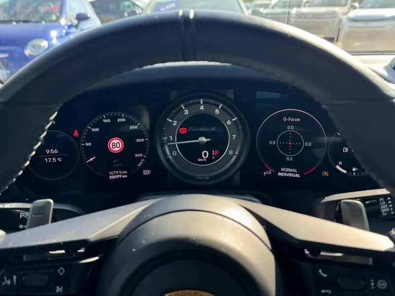 Vue depuis le volant cuir noir du tableau de bord numérique de la Porsche 911 Turbo S 3.7 650ch, affichage des compteurs et indicateurs.