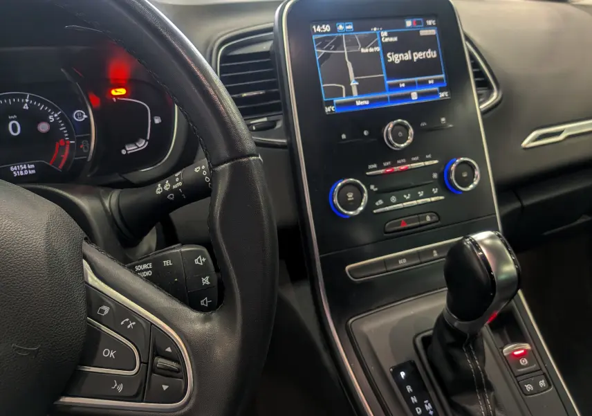 Vue intérieure centrée sur le tableau de bord et levier de vitesse d’un Renault Grand Scenic IV gris Cassiopé, avec écran tactile allumé.