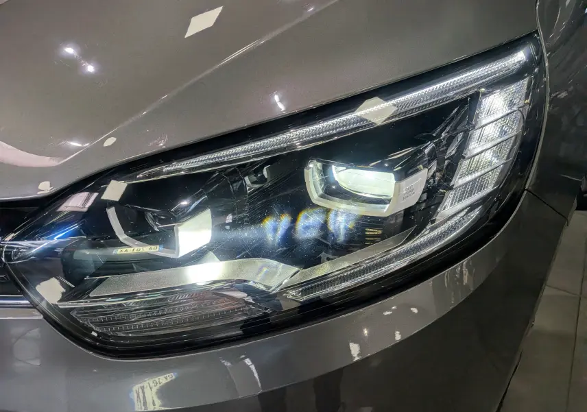 Gros plan sur le phare avant droit du Renault Grand Scenic IV gris Cassiopé, mettant en valeur son design LED moderne.