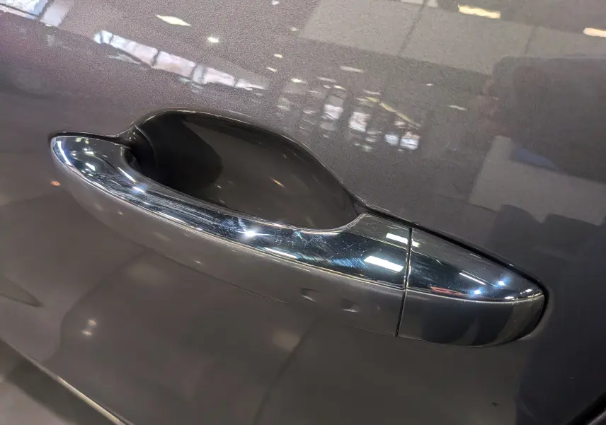 Poignée de porte chromée sur la portière côté gauche d’un Renault Grand Scenic IV gris Cassiopé, reflet intérieur visible.