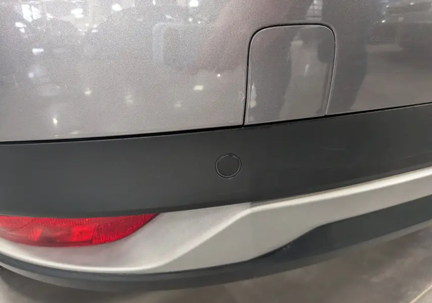 Gros plan sur le pare-chocs arrière gris Cassiopé du Renault Grand Scenic IV avec feu arrière rouge et capteur de recul.