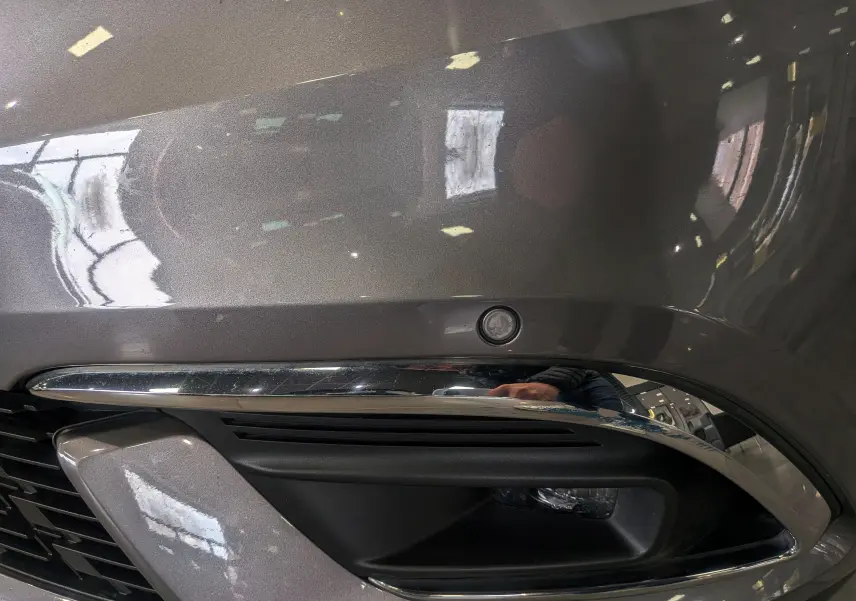 Gros plan sur le pare-chocs avant gris Cassiopé du Renault Grand Scénic IV avec capteur de stationnement et insert chromé.