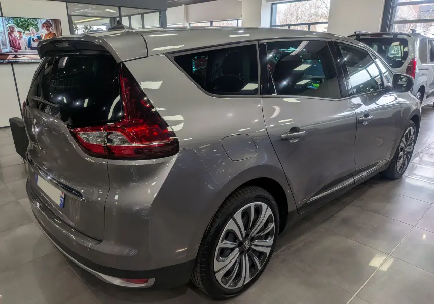 Renault Grand Scenic IV gris Cassiopé vu en 3/4 arrière droit, avec feux arrière distinctifs et jantes stylisées.