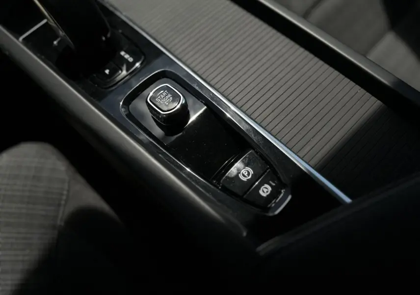 Gros plan sur la console centrale noire du Volvo S60 2024, avec bouton Start/Stop et frein de parking électronique.
