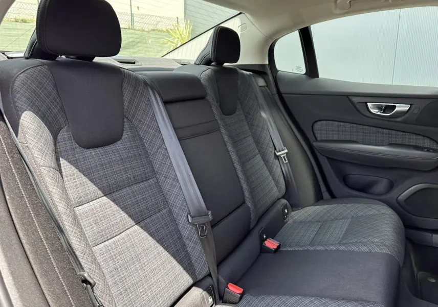 Vue intérieure côté droit des sièges arrière en tissu gris à motifs de la Volvo S60 2024, avec ceinture de sécurité visible.