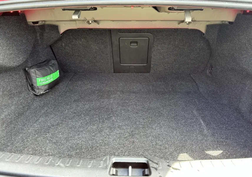 Coffre ouvert d'une Volvo S60 B4 2024 Rouge Fusion, montrant un espace de rangement avec trappe centrale et trousse de secours.
