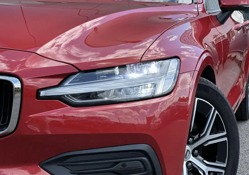 Gros plan sur l'avant droit de la Volvo S60 rouge Fusion 2024, mettant en valeur le phare LED et la jante alliage noire diamant.