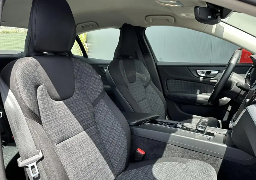 Vue intérieure côté conducteur du Volvo S60 2024, sièges tissu gris à motif carreaux et console centrale moderne.