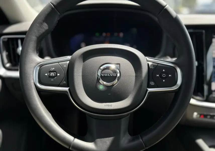 Vue rapprochée du volant noir de la Volvo S60 2024 avec commandes intégrées et logo central brillant.