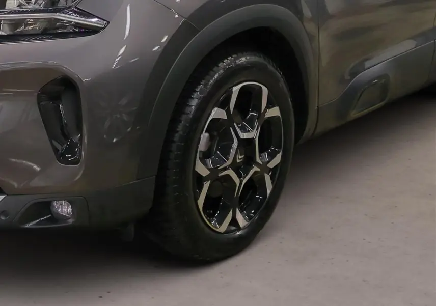 Gros plan sur la roue avant droite et la partie avant grise platinium du Citroën C5 Aircross Hybrid avec jante alliage bicolore.
