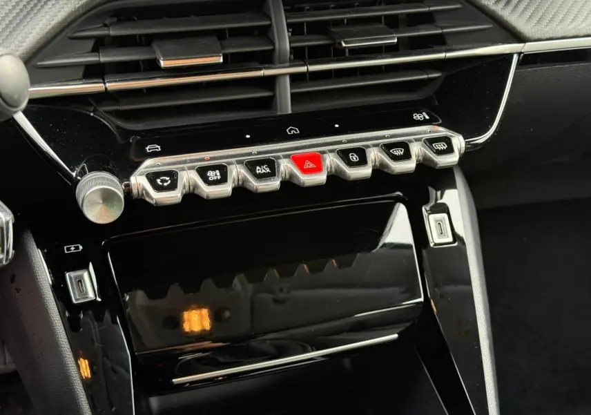 Vue rapprochée de la console centrale noire brillante de la Peugeot 208 1.2 100ch Allure avec ses commandes tactiles et boutons métalliques.