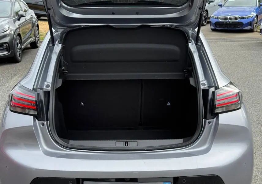 Coffre ouvert d’une Peugeot 208 gris Artense vue de l’arrière, avec feux arrière LED allumés.