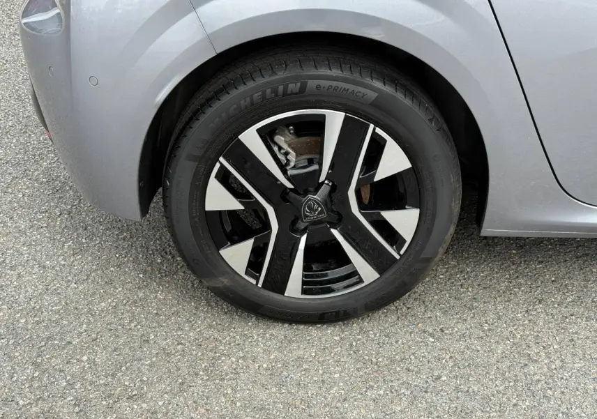 Gros plan sur la roue avant gauche d'une Peugeot 208 gris Artense avec jante alu noire et argentée.