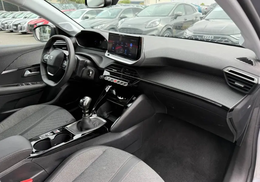 Intérieur avant droit de la Peugeot 208 1.2 100ch gris Artense, avec tableau de bord moderne et écran tactile central.