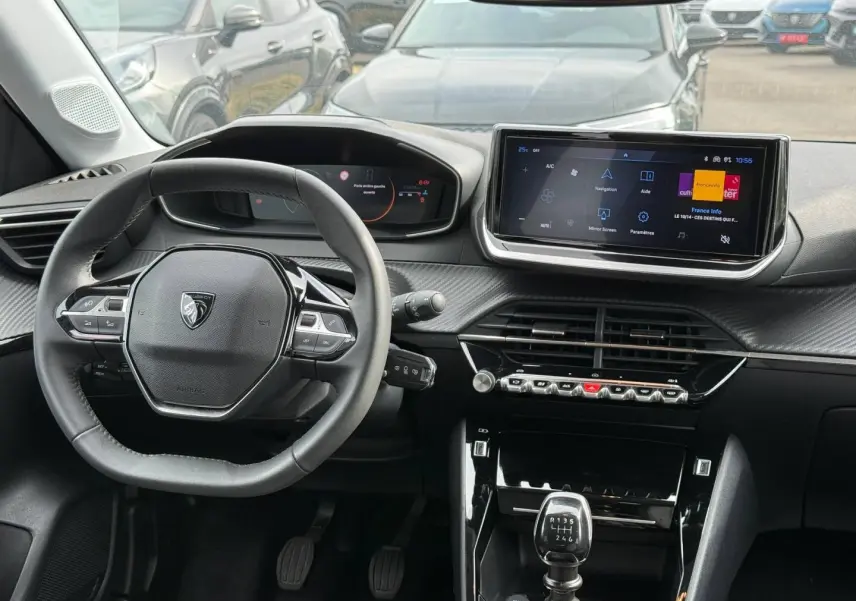 Vue intérieure avant de la Peugeot 208 gris Artense, volant compact, écran tactile et levier de vitesses manuel visibles.