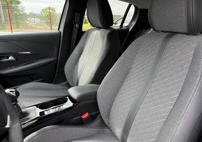 Vue intérieure côté avant droit des sièges tissu gris avec surpiqûres et accoudoir central de la Peugeot 208 1.2 100ch 2025.