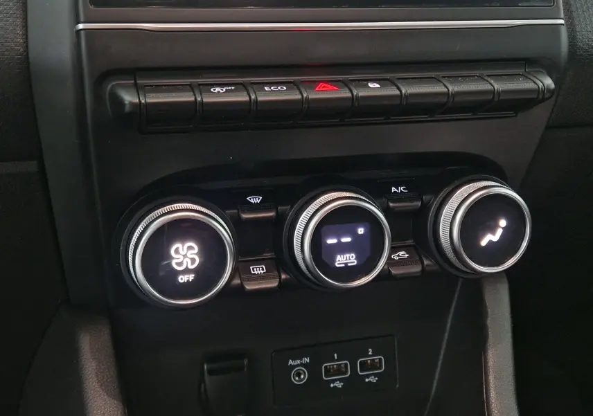 Gros plan sur les commandes de climatisation et les boutons de fonction du tableau de bord d’une Renault Clio V gris platine.