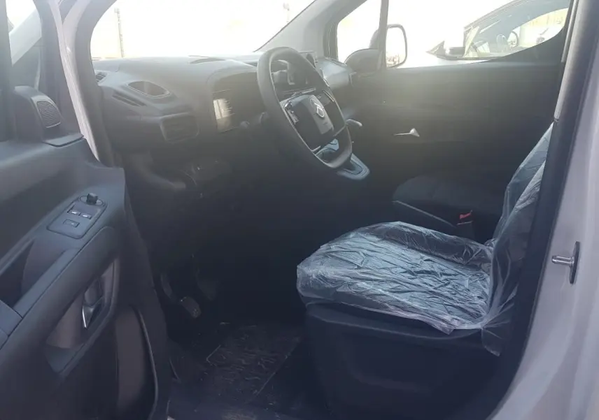 Vue intérieure côté conducteur du Citroën Berlingo blanc 2025, volant multifonctions et siège protégé par housse plastique.
