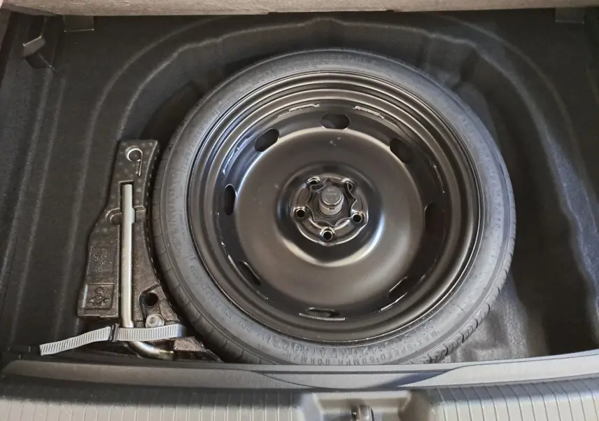 Roue de secours en acier noir avec clé de roue, vue de dessus dans le coffre d'une Volkswagen Golf 2025.