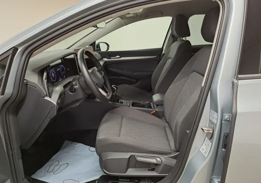 Vue intérieure côté conducteur de la Volkswagen Golf 1.5 eTSI 2025 argent Dolomite, sièges tissu gris et tableau de bord numérique.