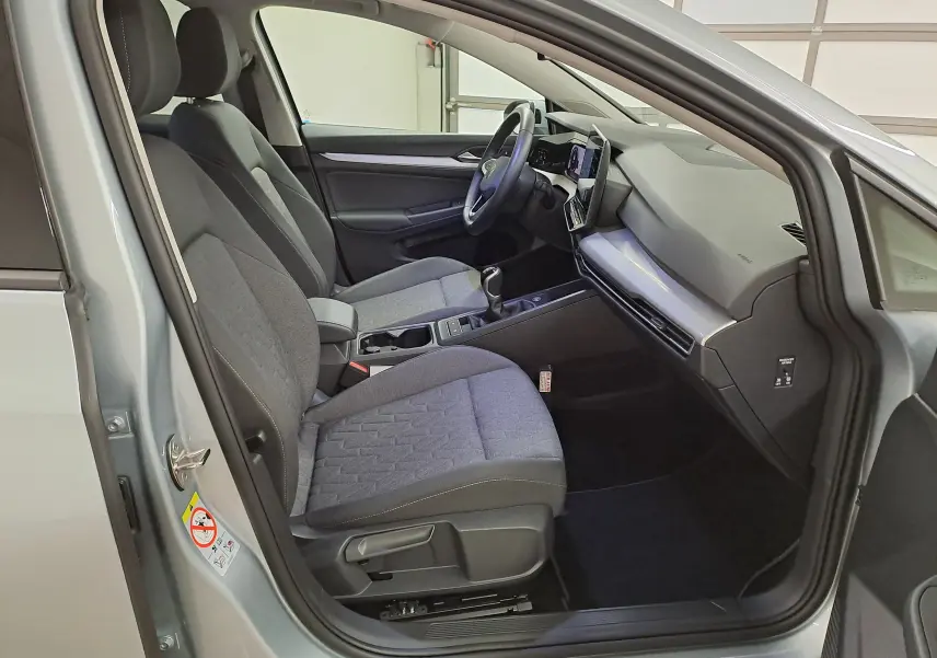 Vue intérieure côté conducteur d'une Volkswagen Golf 1.5 eTSI 116 BVM6 argent Dolomite, avec sièges tissu gris et tableau de bord moderne.