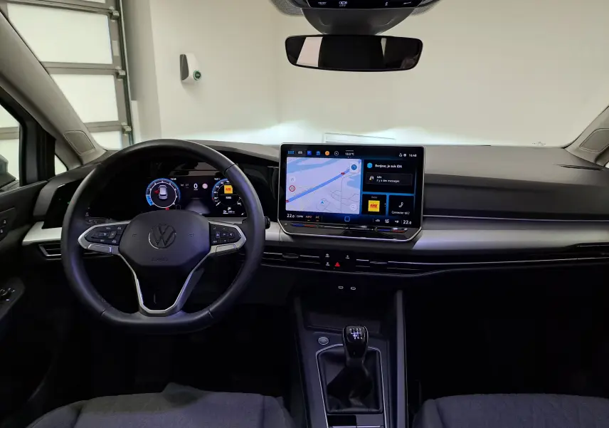 Vue intérieure avant du tableau de bord de la Volkswagen Golf 1.5 eTSI 2025 avec écran tactile et volant multifonction noir.